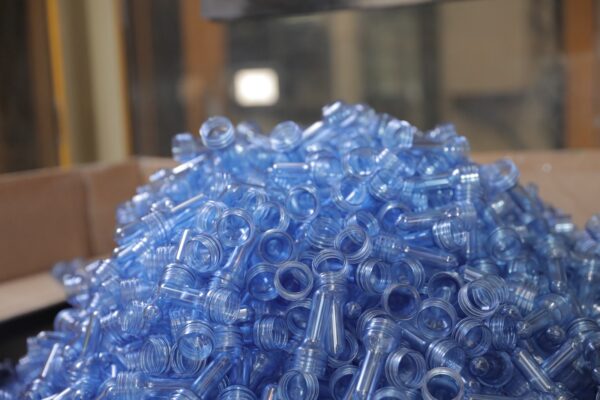 A large pile of blue plastic bottle caps is stacked together, reflecting light in a factory setting 