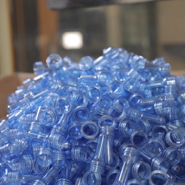 A large pile of blue plastic bottle caps is stacked together, reflecting light in a factory setting 