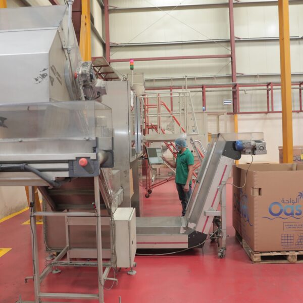 A worker in a green shirt operates machinery in a warehouse, with large boxes labeled "Oasis" in the background 