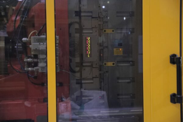 A close up of industrial machinery with a yellow frame, featuring control panels and digital displays behind glass 