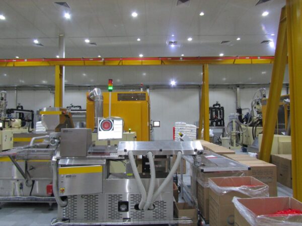 A spacious industrial facility with various machines, including packaging equipment and storage boxes, under bright lighting 